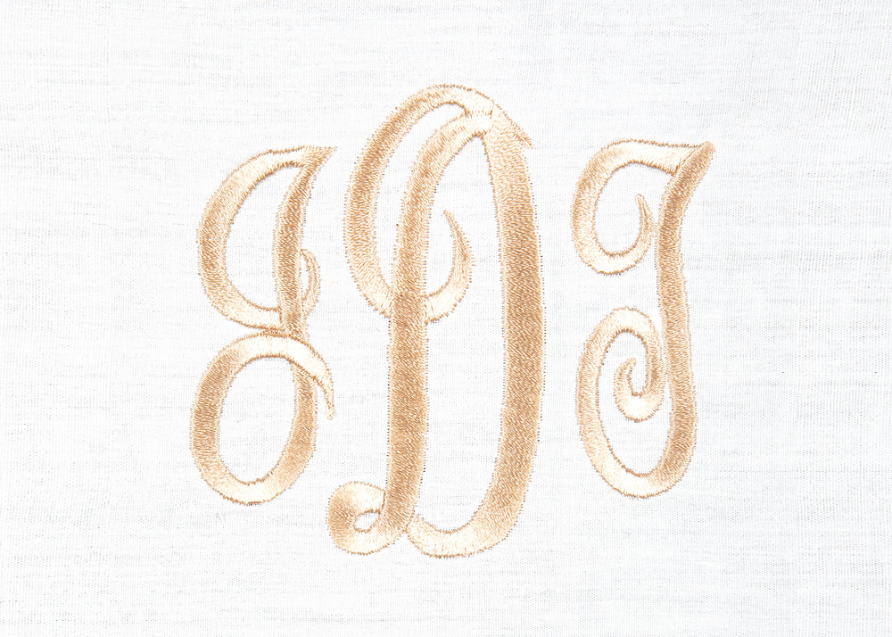 Close-up of white cotton dinner napkin showcasing gold embroidered three-letter monogram on textured waffle-weave fabric