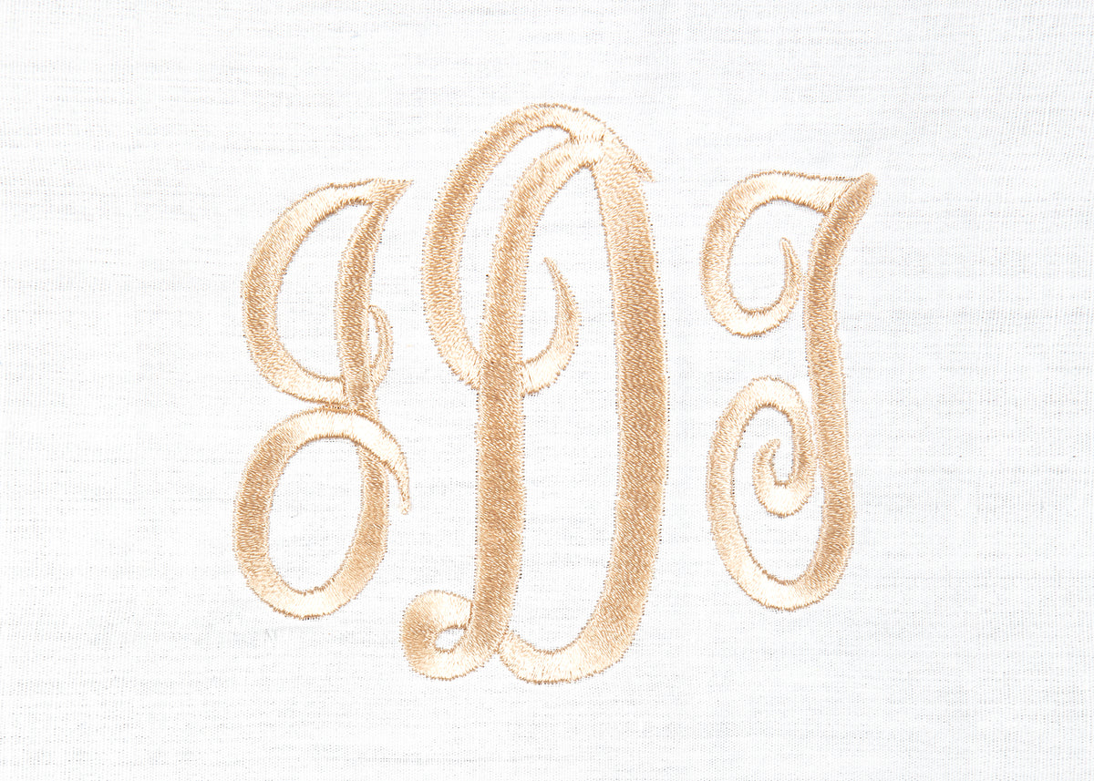 Close-up of white cotton dinner napkin showcasing gold embroidered three-letter monogram on textured waffle-weave fabric