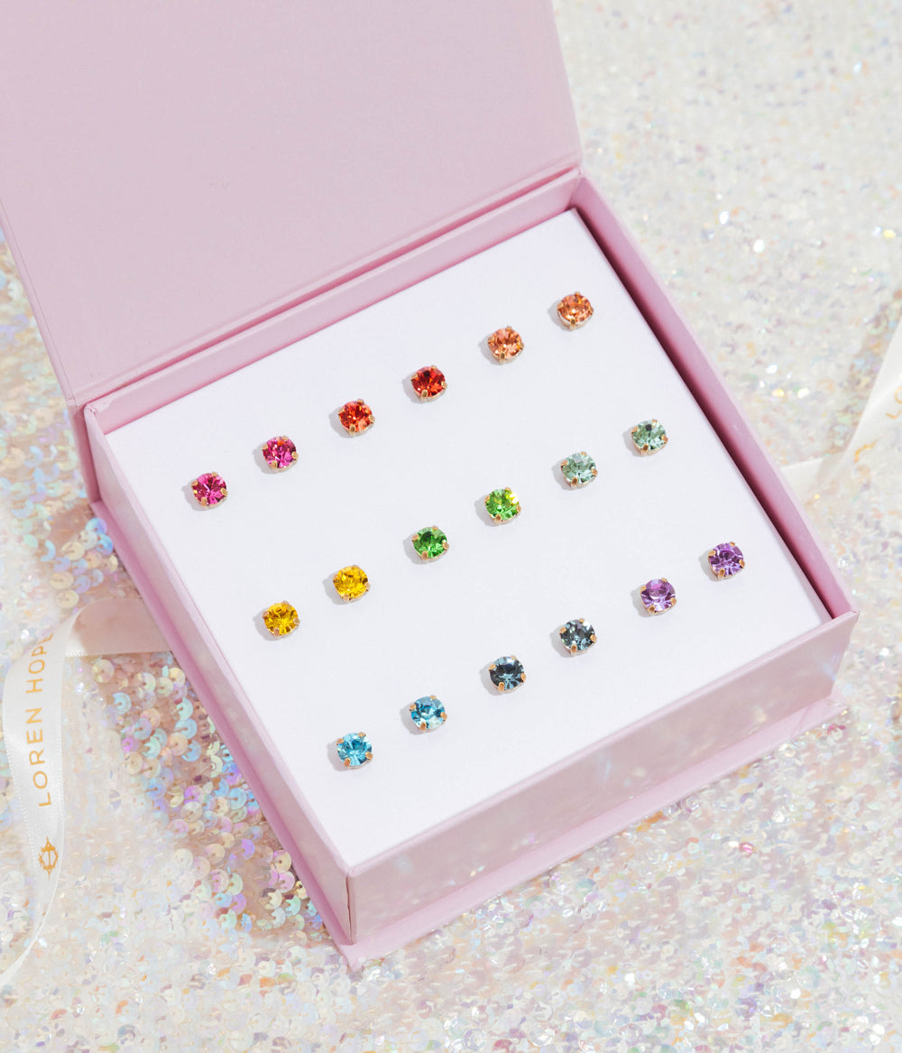 Top-down view of Rainbow Bright stud set showing multicolored crystal studs in a pink gift box on an iridescent sequin background