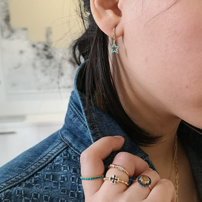 Close-up of star charm earrings on model: 18K gold hoops with turquoise cabochons and diamonds, shown against a denim jacket