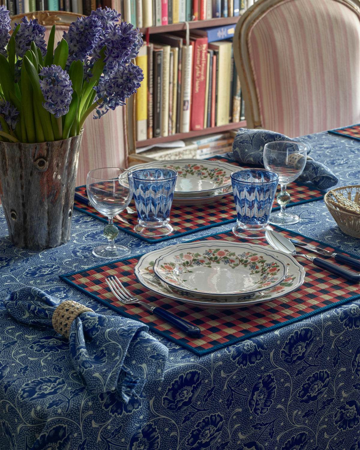 Angled view of Capri Placemat, Red and Blue showcasing its handwoven checkered pattern with a set dining table background