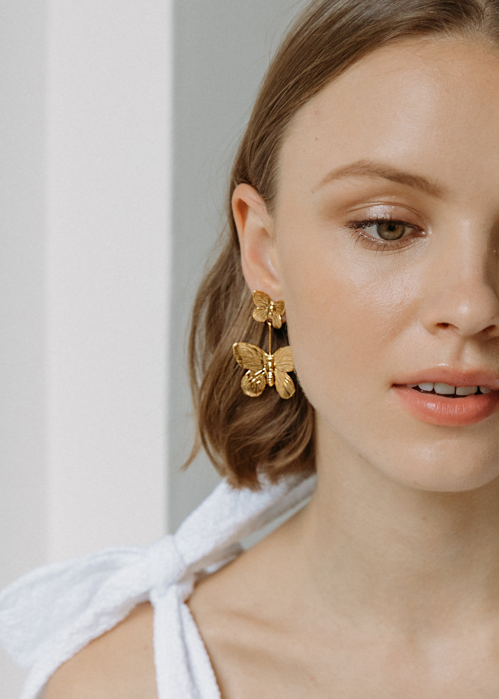 Close-up of Ella Earrings showcasing gold double-butterfly drop design on model with soft white background