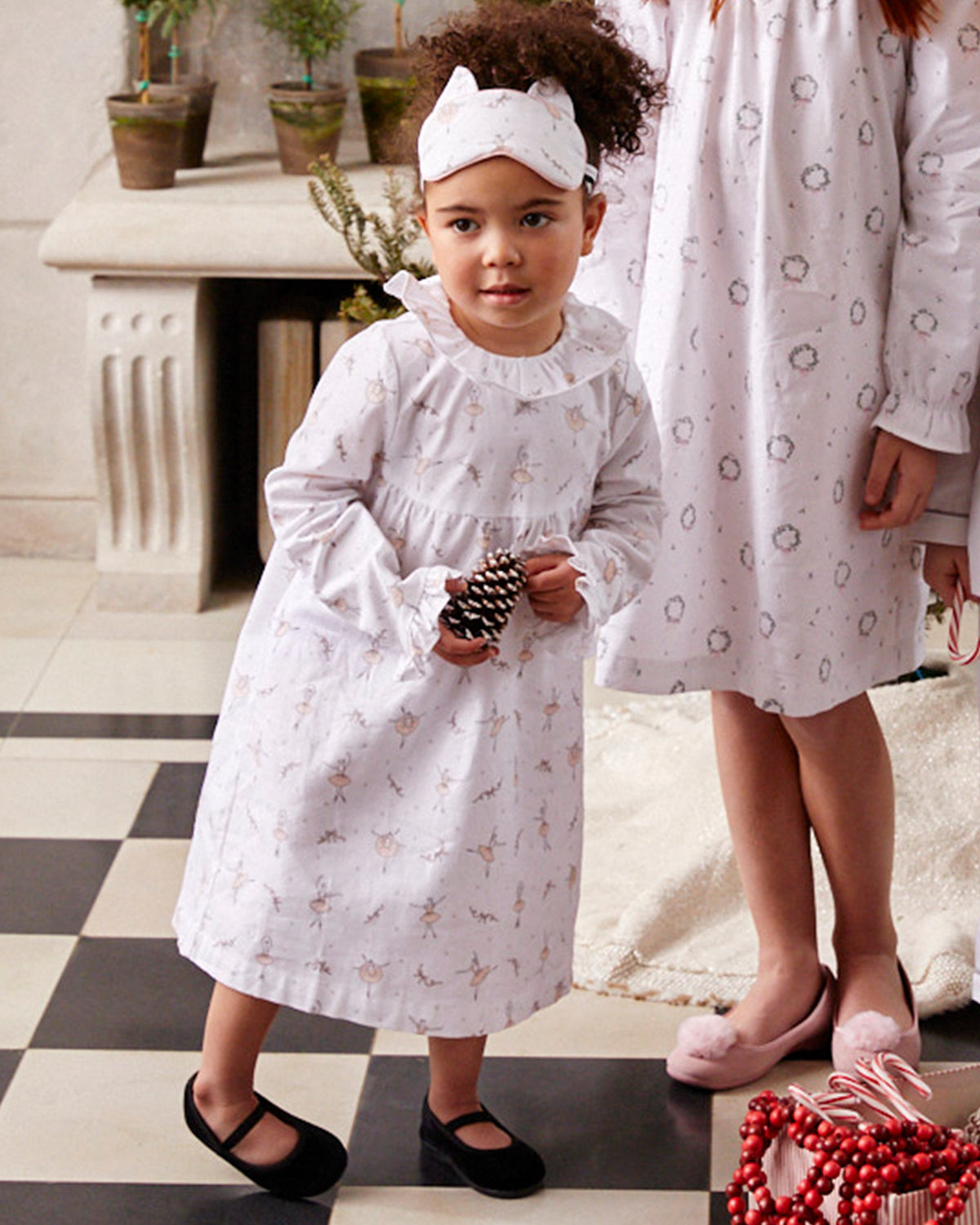 Front view of The Delphine Slipper in Black Velvet showcasing black velvet footwear on a child indoors