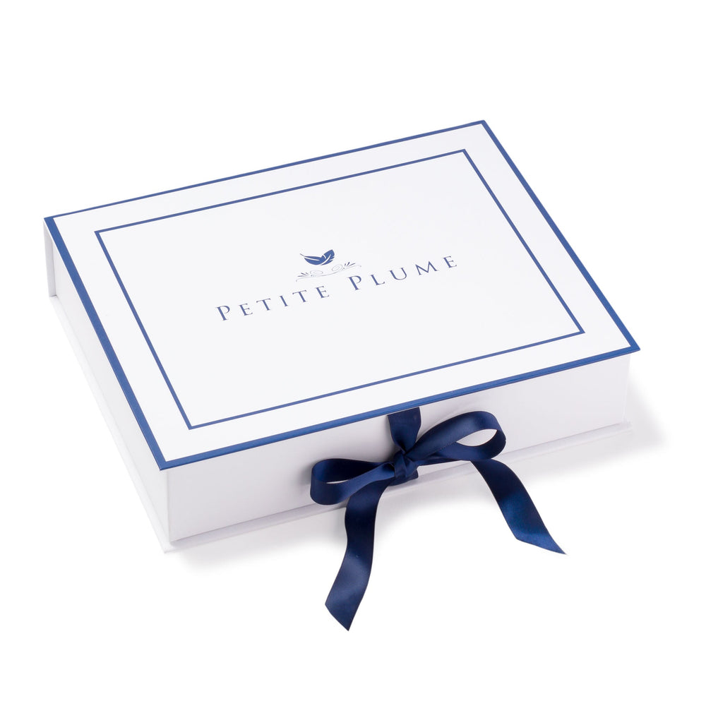 Angled view of Petite Plume gift box showing blue border, centered logo, and tied navy ribbon on white background