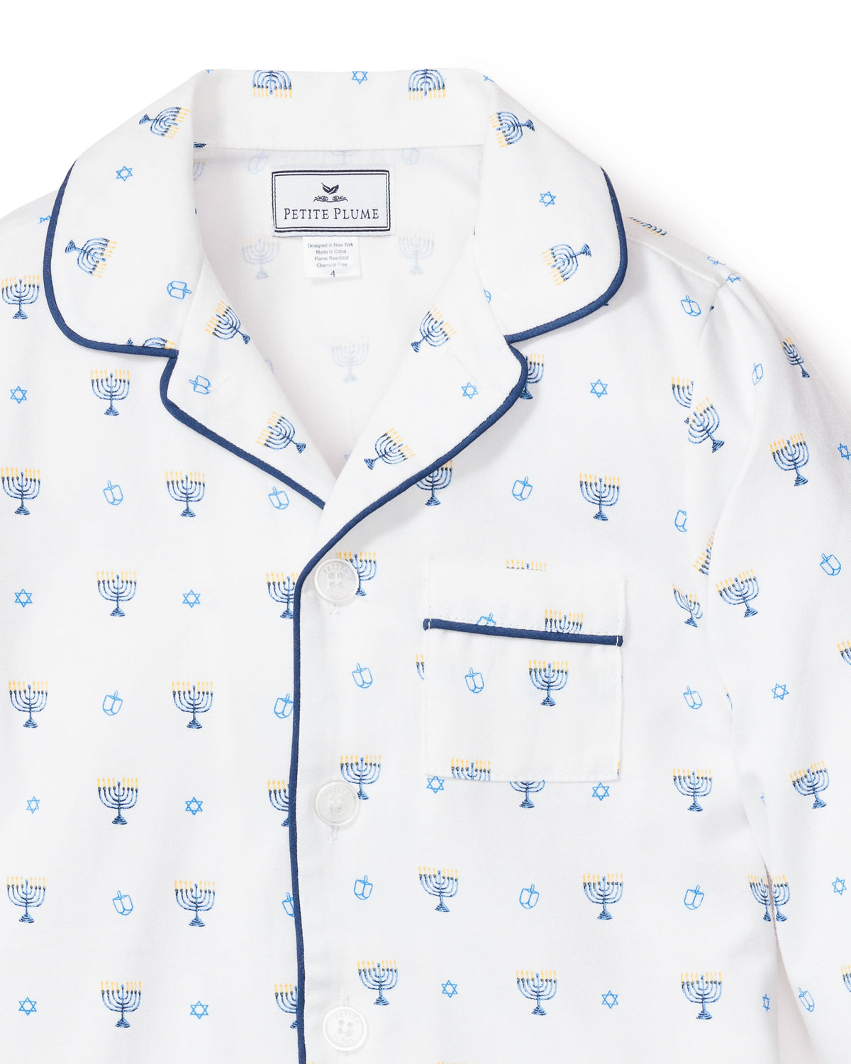 Front close-up of children’s Hanukkah pajama top showing blue-and-yellow menorah and dreidel print, navy piping on white