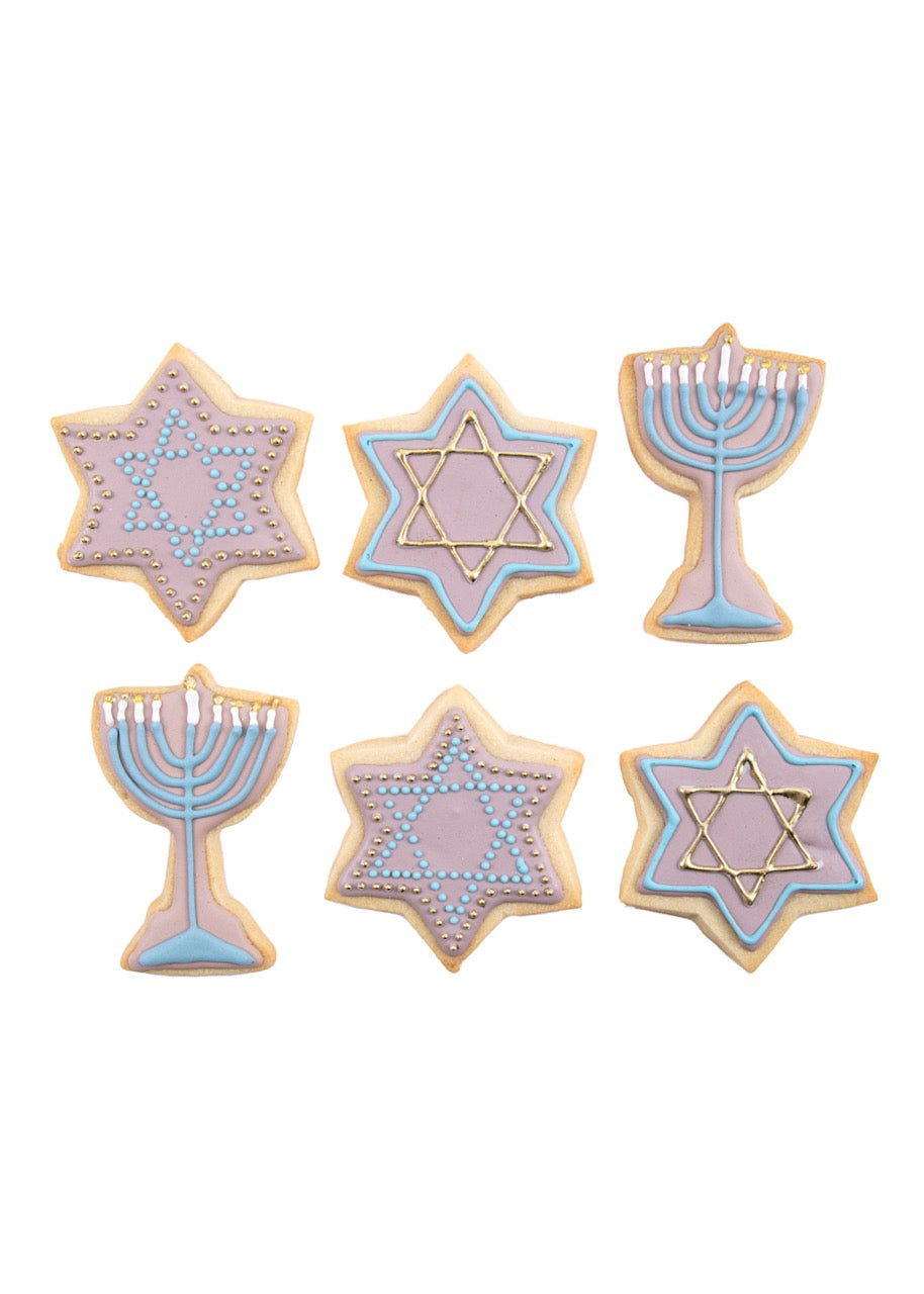 Flat lay view of six Menorah and Star of David sugar cookies with pastel purple, blue and gold royal icing on white background
