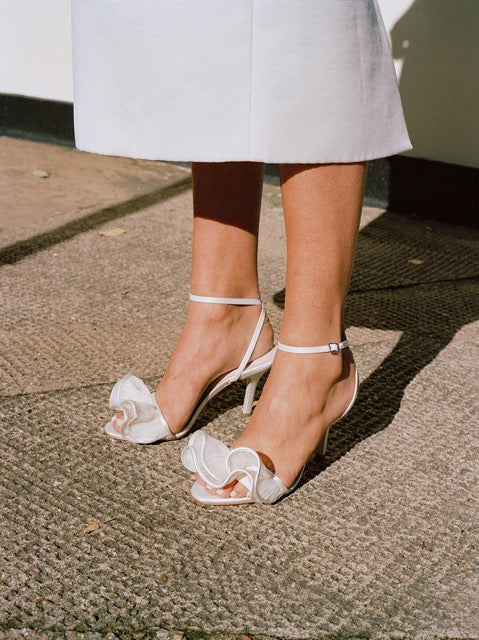 Close-up view of Estella sandal in vegan pearl organza showcasing ankle straps and gathered toe details against a textured outdoor surface
