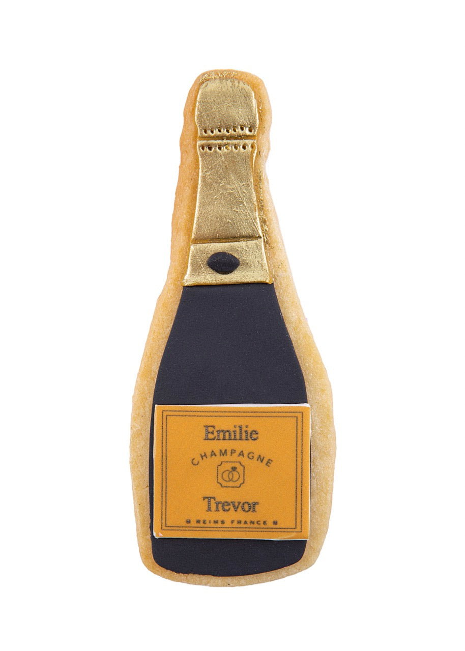 Front of champagne bottle sugar cookie with gold-foiled neck, black fondant and orange label reading Emilie and Trevor