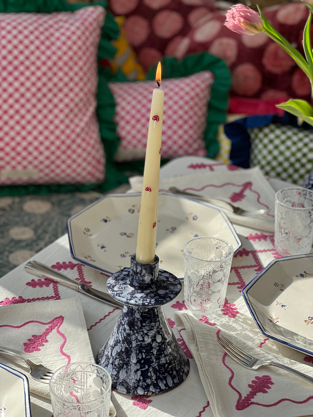 Table set on Indian pink vine tablecloth with lit taper candle in blue speckled holder and floral plates