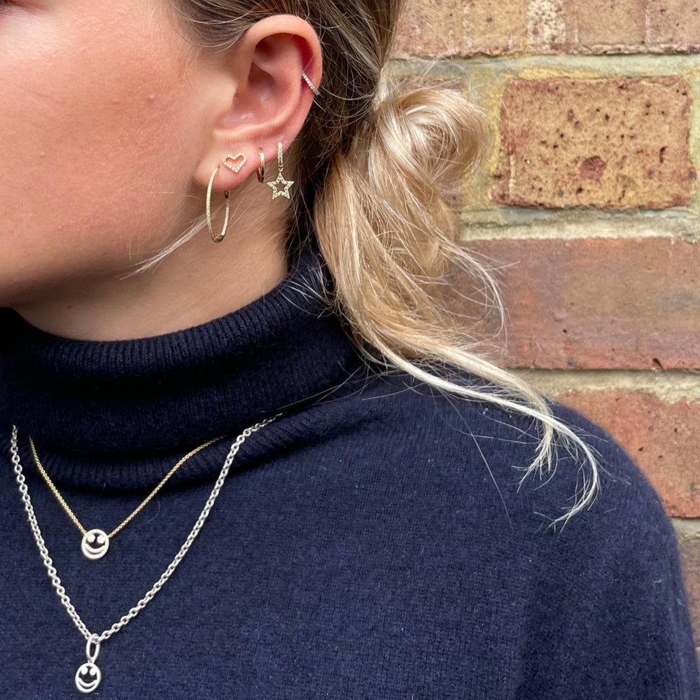 Side view of 1 inch gold diamond hoop earrings on a model’s ear showcasing pave diamonds with a brick wall background