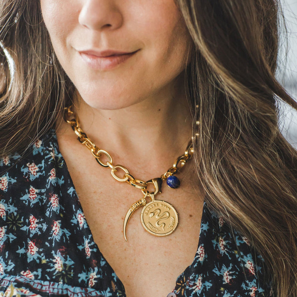 Close up of chunky gold link choker showing a lapis bead and coin pendants on a model wearing a patterned blouse