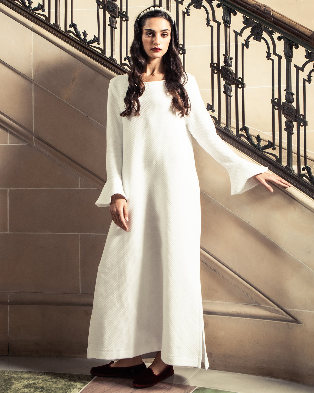 Woman wearing Bordeaux velvet loafers and a white robe on an ornate staircase