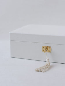 White Italian leather wedding day keepsake box shown closed with gold key with white tassel inserted into a key lock. 