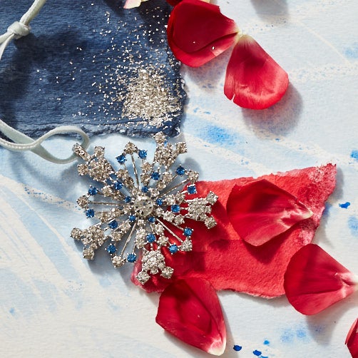 Close-up of Sparkle Snowflake Ornament in Sapphire showcasing shimmering blue and silver details with a painted blue backdrop