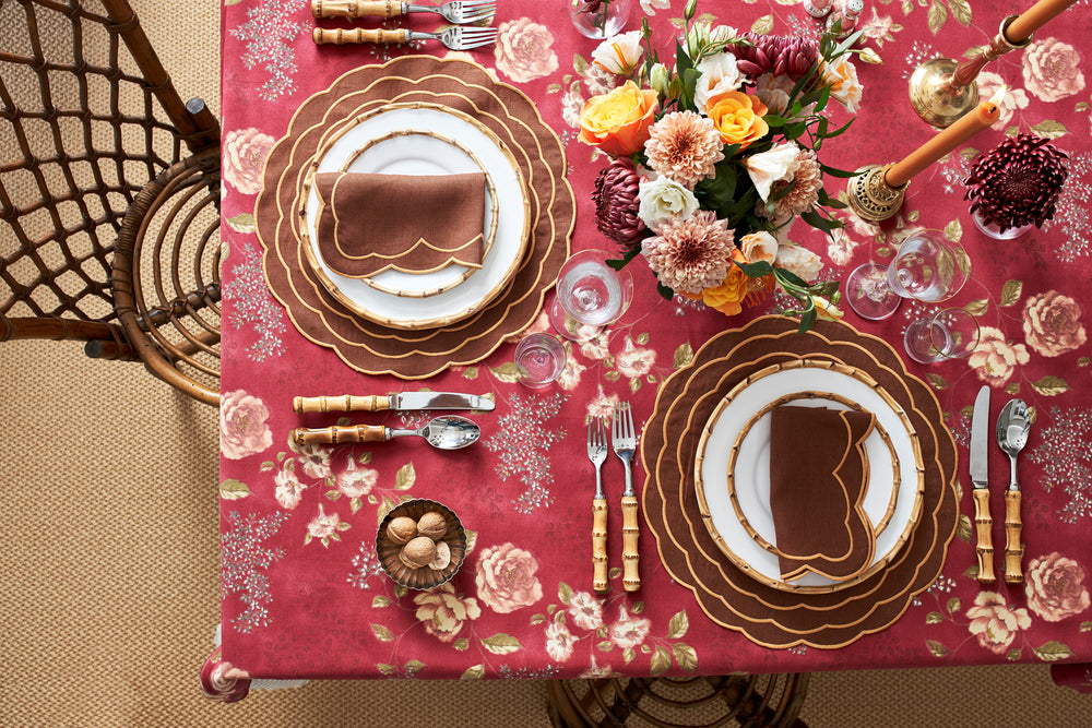 Table set with tabac scalloped placemats embroidered with marigold, bamboo-handled flatware and a peach floral centerpiece