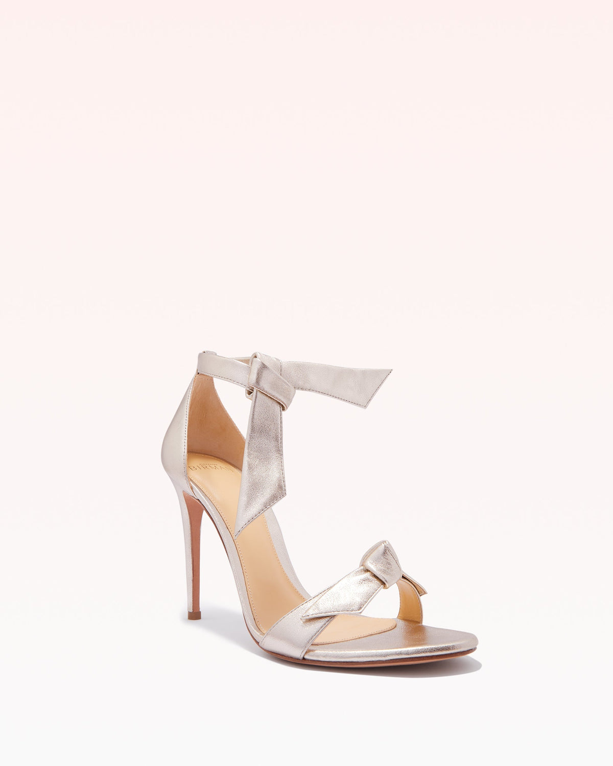 Three quarter view of Clarita 100 in Golden Leather showcasing two bow accents and stiletto heel on a pale background