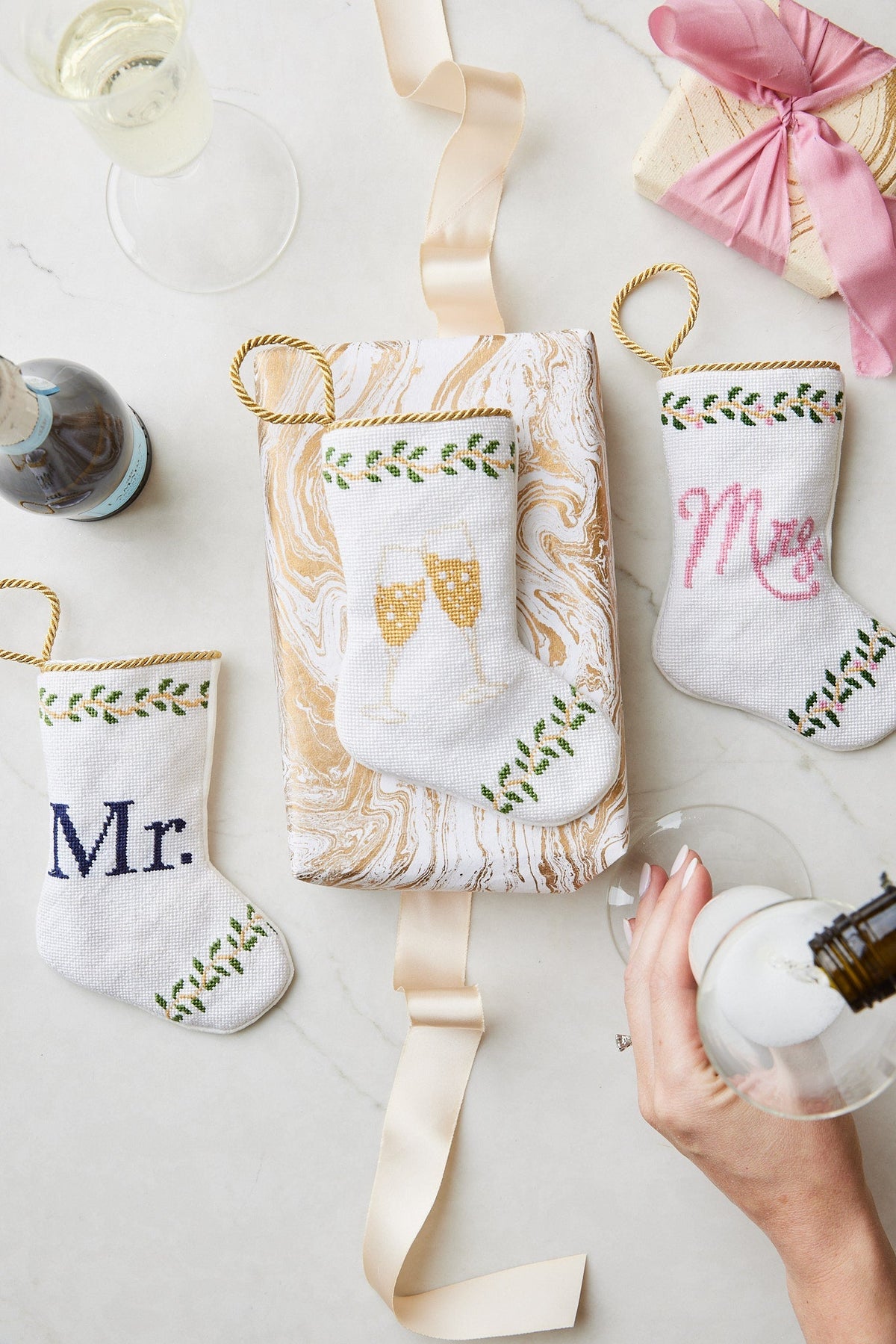 Front view of Champagne Toast Bauble Stocking showcasing needlepoint champagne glasses and gold rope hanger on a gift box