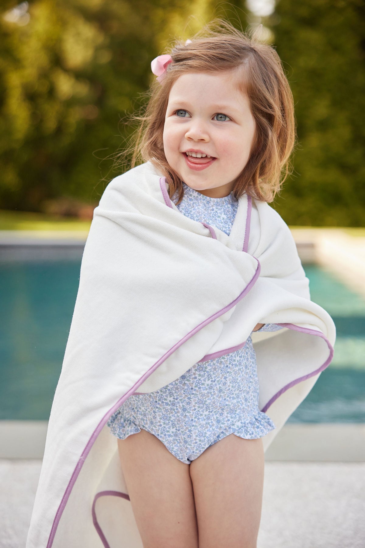 Front view of Piped Hooded Bath Towel and Washcloth Set in sand with lavender piping wrapped around a toddler by a pool