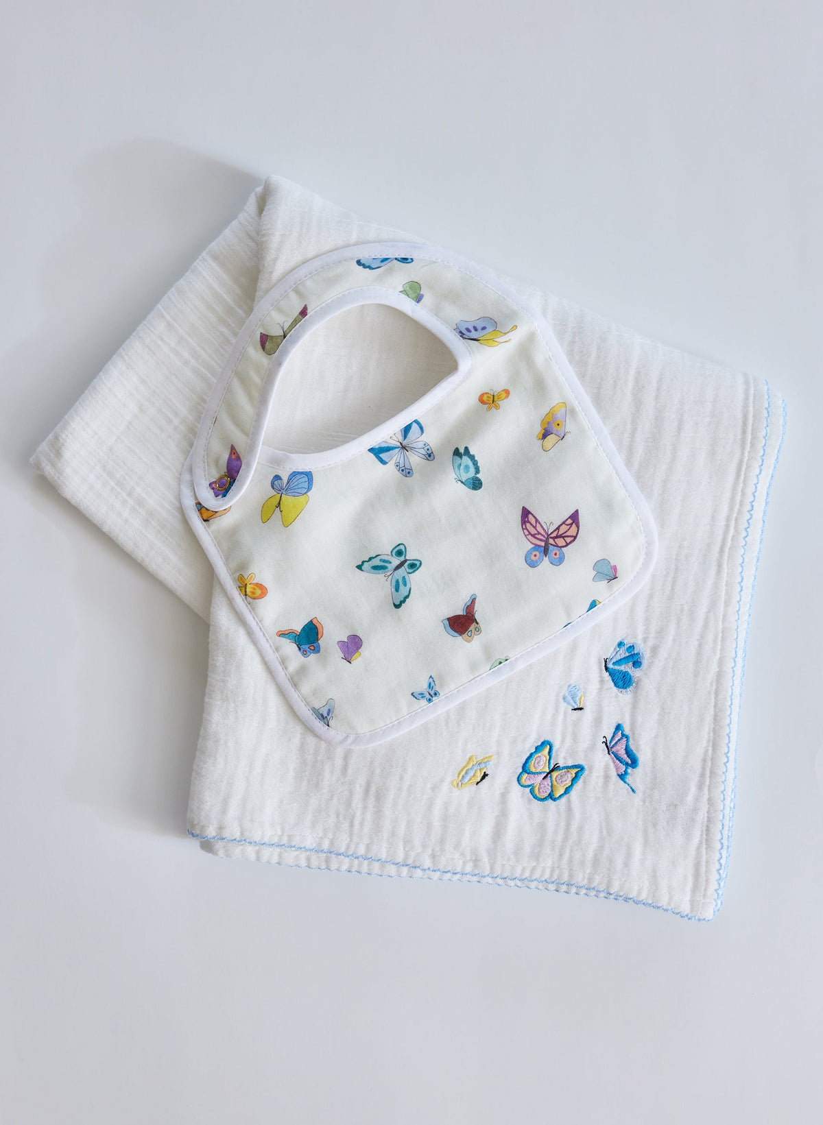 Top view of Madame Butterfly bib and shawl blanket set showcasing colorful butterfly designs and embroidered details on white fabric