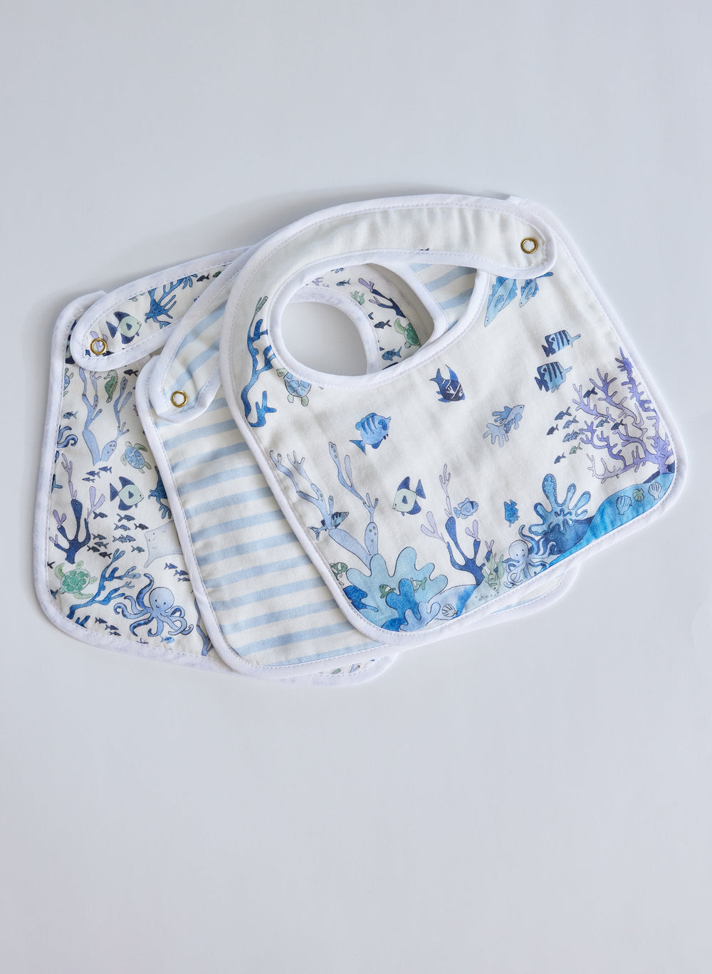 Top view of Under the Sea bib set showing three cotton baby bibs — two blue ocean-print and one blue-and-white striped — on a white background