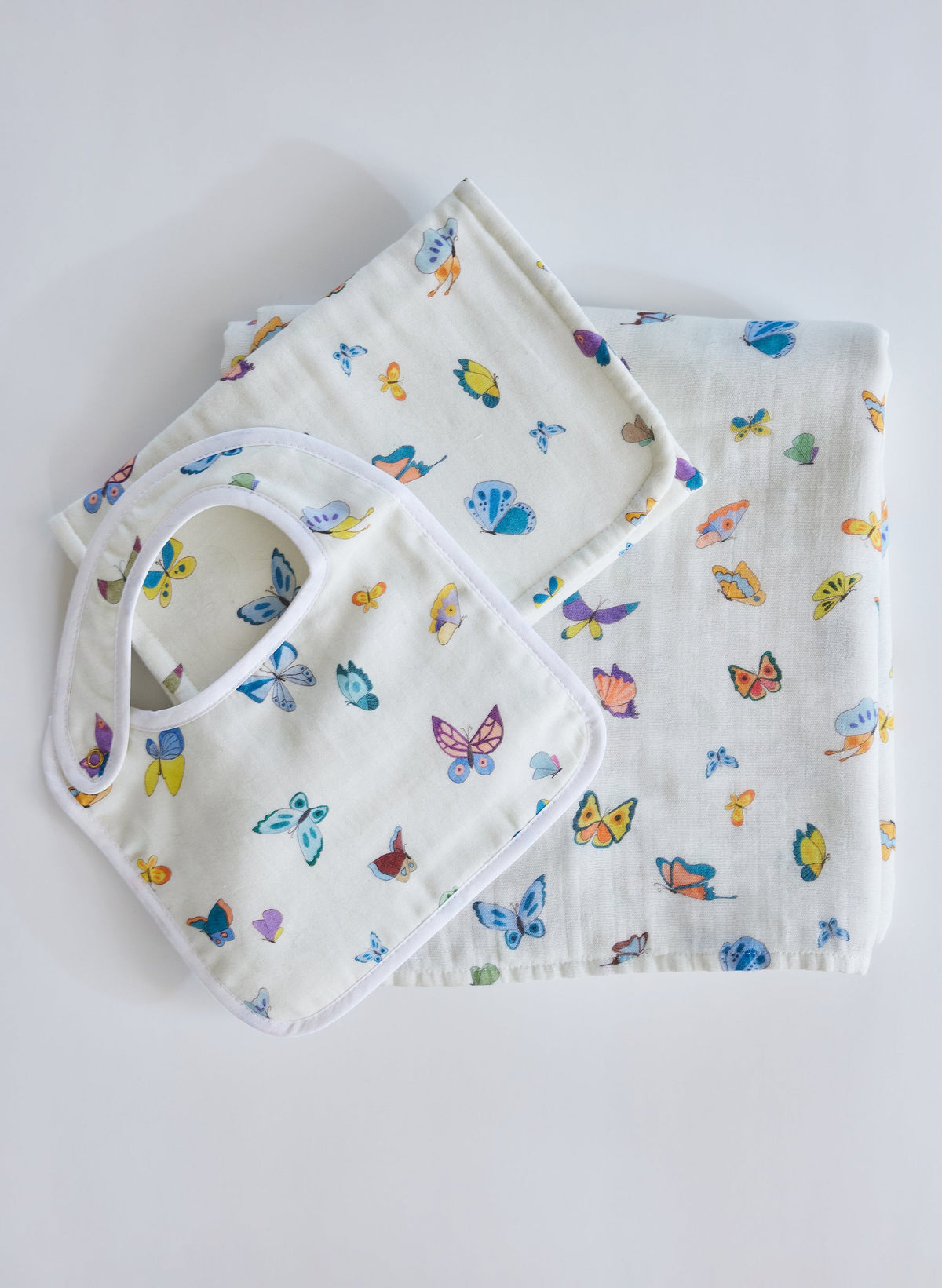 Overhead view of Madame Butterfly Bundle Set showcasing butterfly print on bib, shawl blanket, and burp cloth on a white background