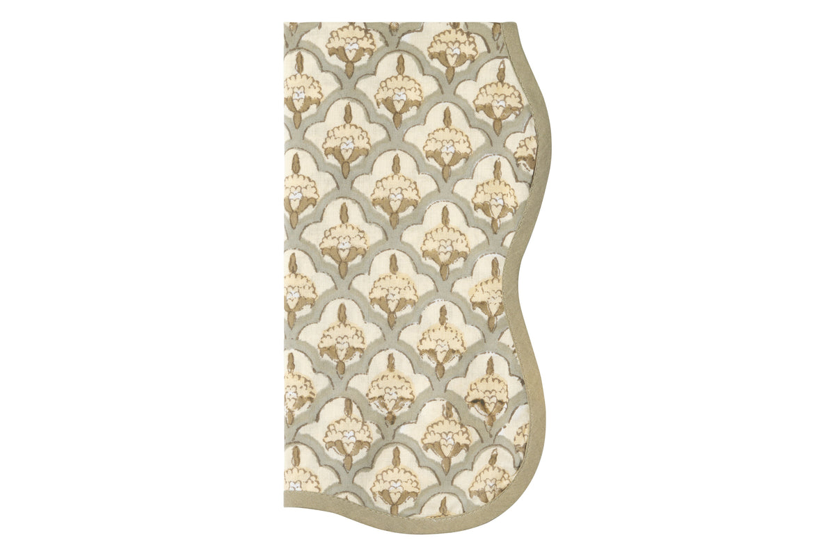 Top view of The Lisbet napkin showcasing mustard yellow floral print and muted green scalloped edge on white background