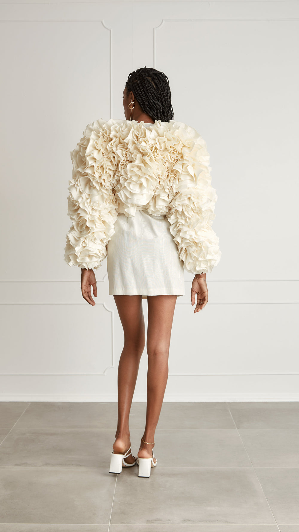 Rear view of Miranda Bolero showcasing ivory layered ruffles and voluminous puff sleeves on a neutral paneled wall