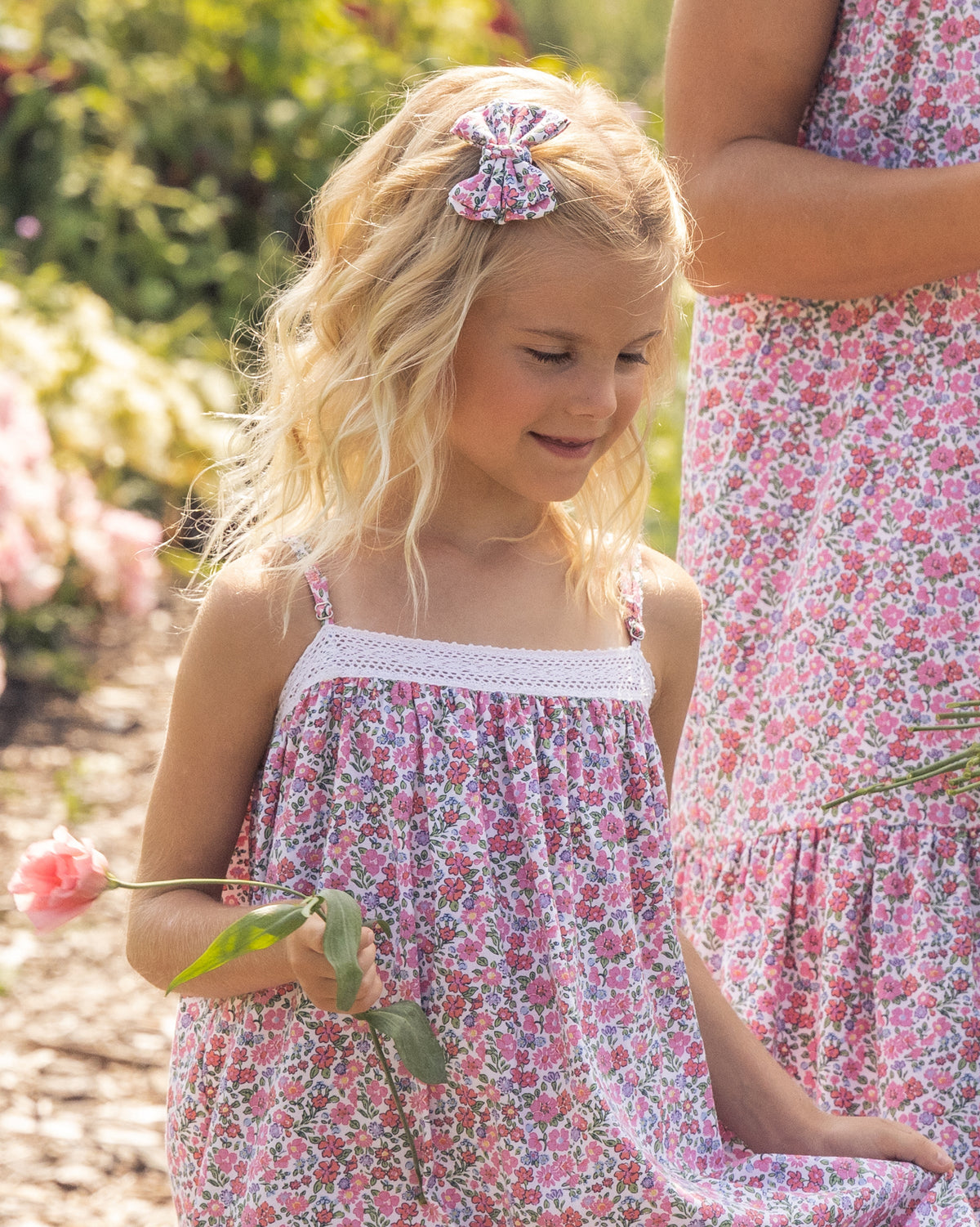 Girl wearing a floral dress and pink floral hair bow outdoors in a garden