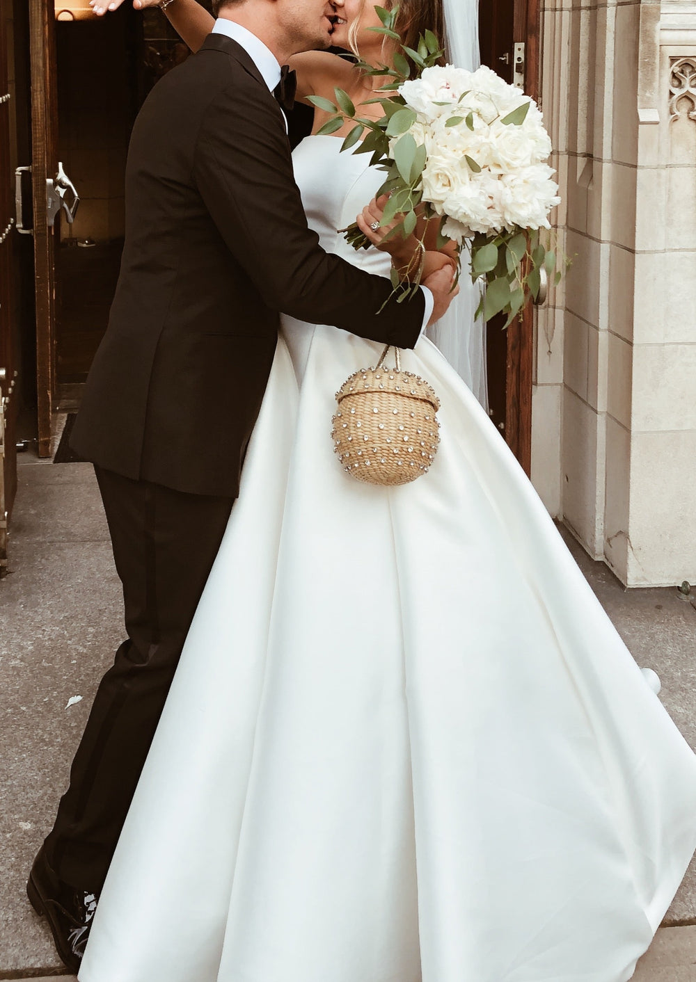 Bride in white wedding gown holding The Disco Ball beaded round wristlet while embracing groom at a church entrance