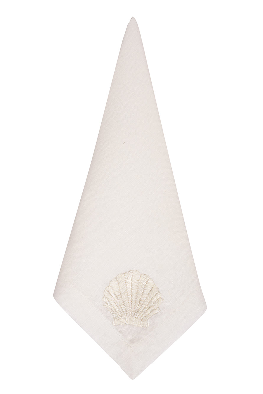 Front view of folded Conchas Mix white linen table napkin showcasing embroidered seashell motif on plain white background
