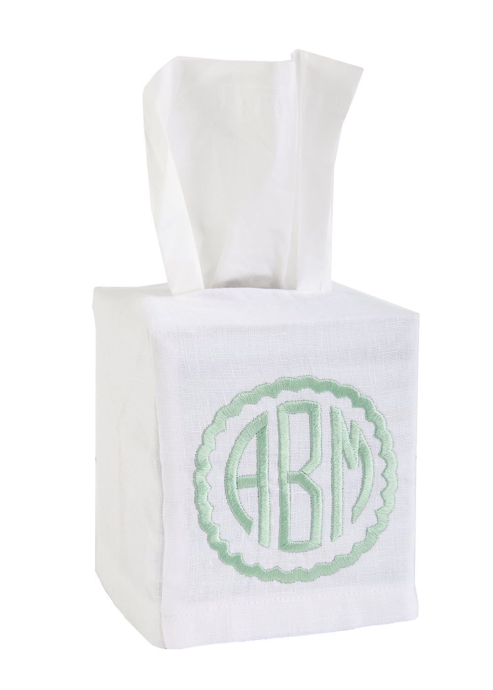 Three-quarter view of white linen tissue box cover showing mint-green monogrammed crest on front with white background