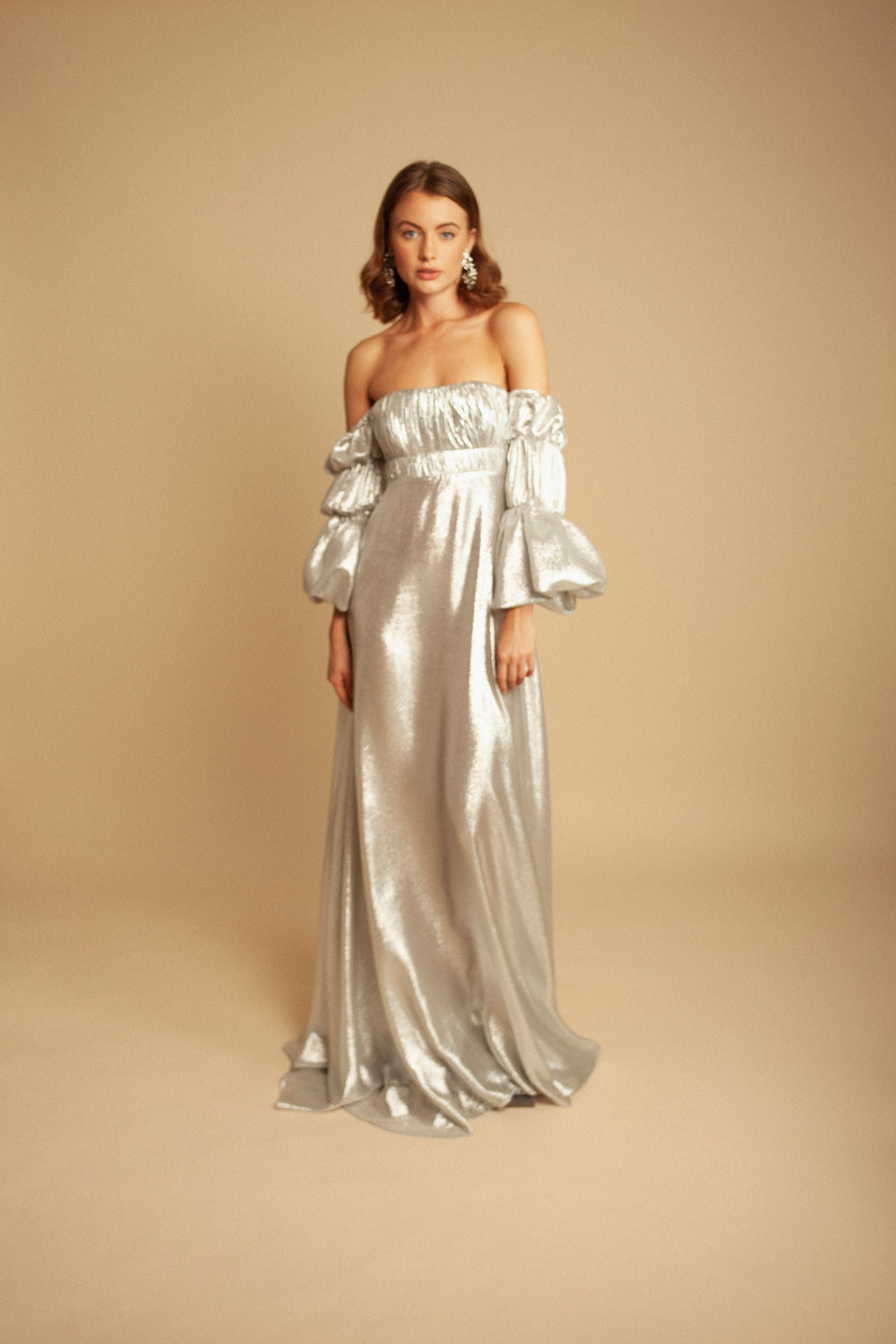 Front view of Plata Dress showcasing off-the-shoulder neckline and puff sleeves in silver lurex on a beige studio background