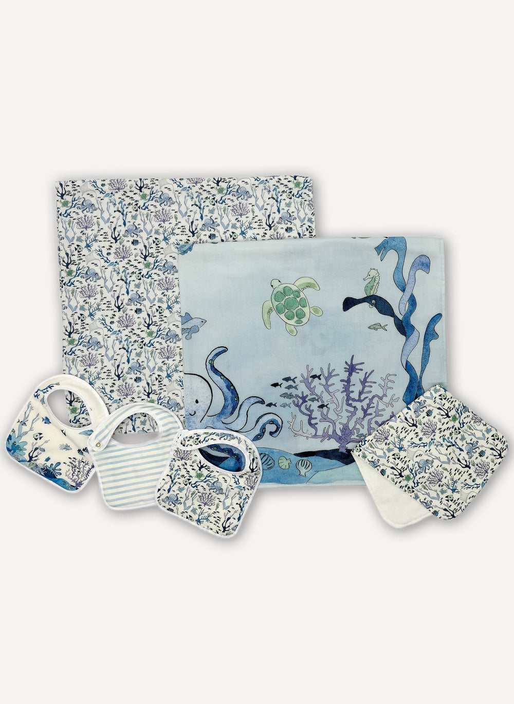 Flat lay of Under the Sea and Coral Reef set: two shawl blankets, three bibs, and a burp cloth with ocean prints on white