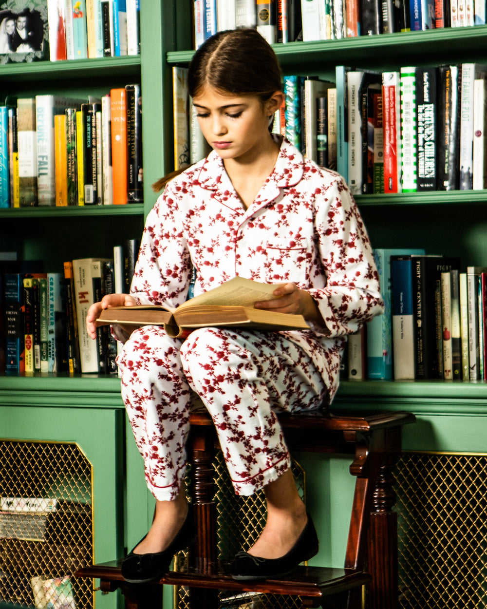 Angled view of Juliette ballet slipper in black velvet worn by model showcasing bow detail and round toe with bookshelf background