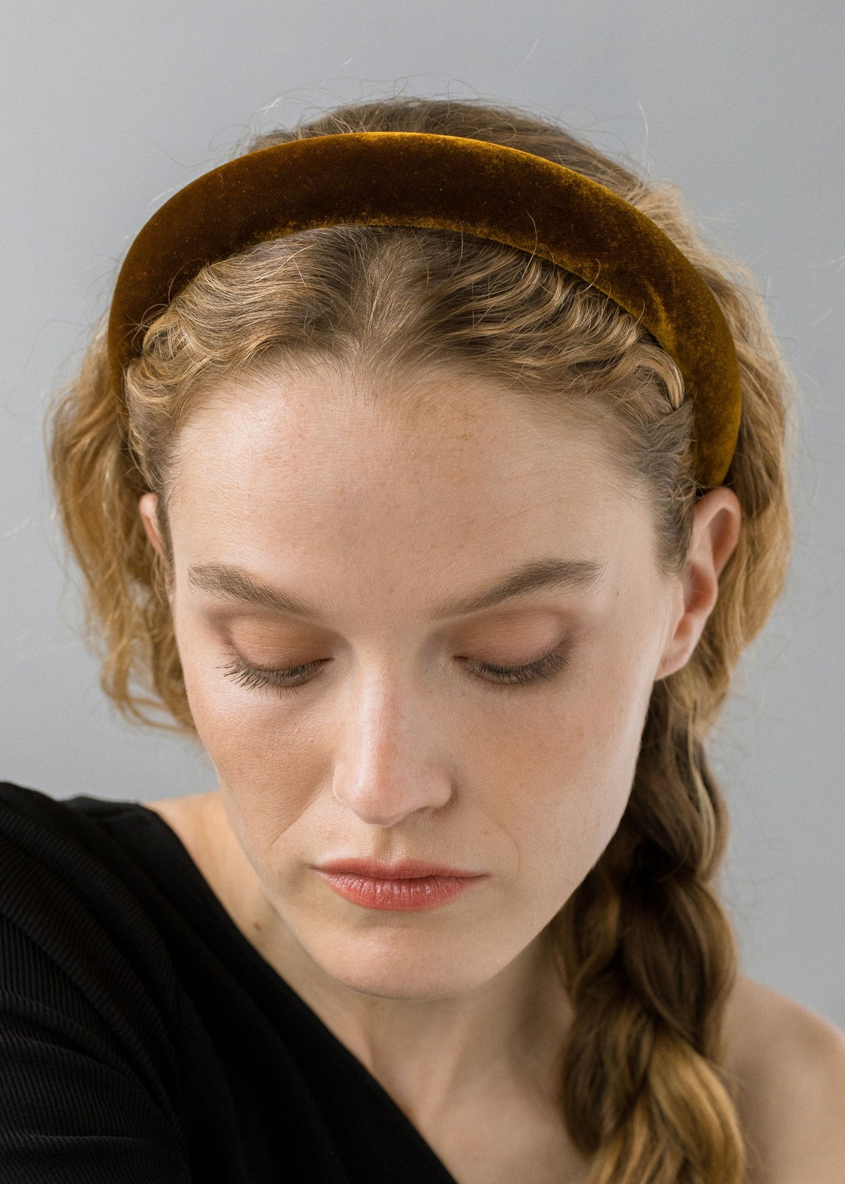 Close-up front of Tori headband in topaz velvet on model, showing padded band and braided hair against a gray background
