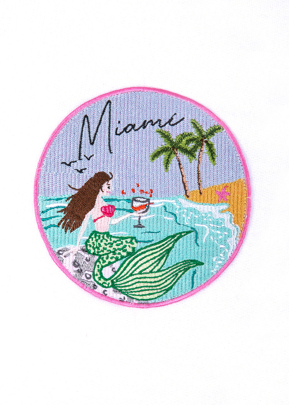 Front view of circular embroidered Miami mermaid patch showcasing green striped tail, palm trees, cocktail glass, and pink border on white background