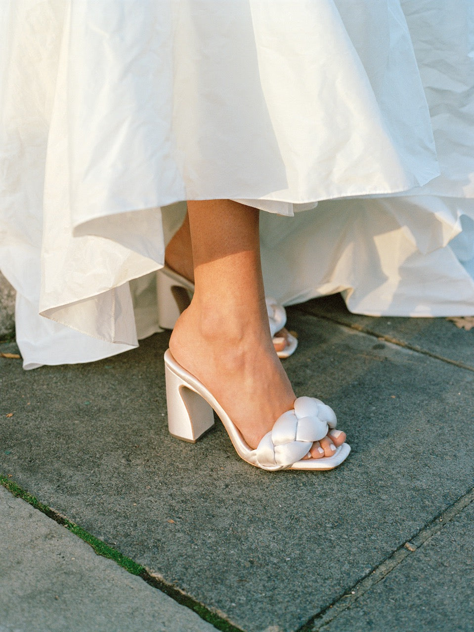 Close-up view of Freya Mule in Cream Satin showcasing wide braided padded footbed and curved heel on a sidewalk