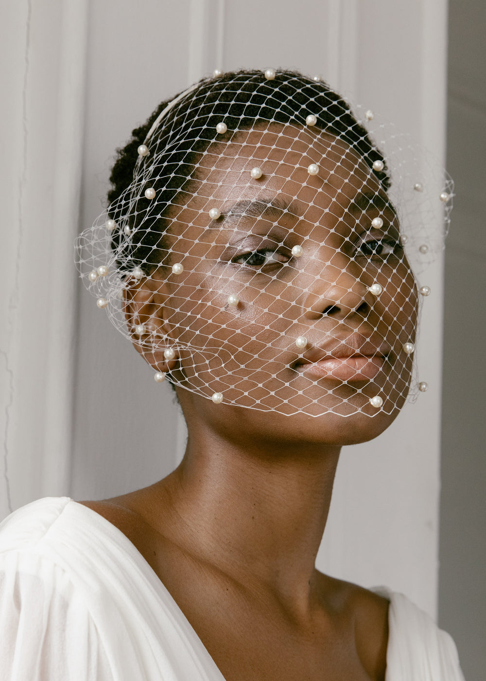 Three-quarter view of Voilette Headband with Pearls on model showing ivory nylon veil dotted with faux pearls against a neutral draped background
