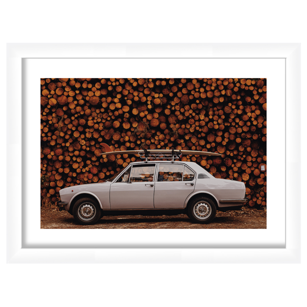Side view of Hossegor framed print showing a vintage sedan with a surfboard on its roof against stacked logs, white frame