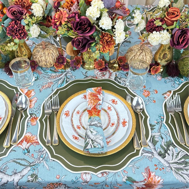 Teal blue tablecloth with gray and white branches, orange and wine flowers and green leaves, and olive placemats and leaf napkin rings