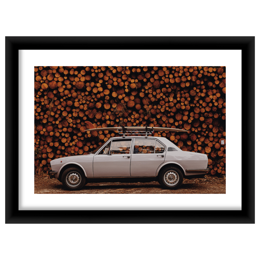 Side view of Hossegor framed print showcasing a vintage white sedan with a surfboard on its roof against stacked logs in a black frame