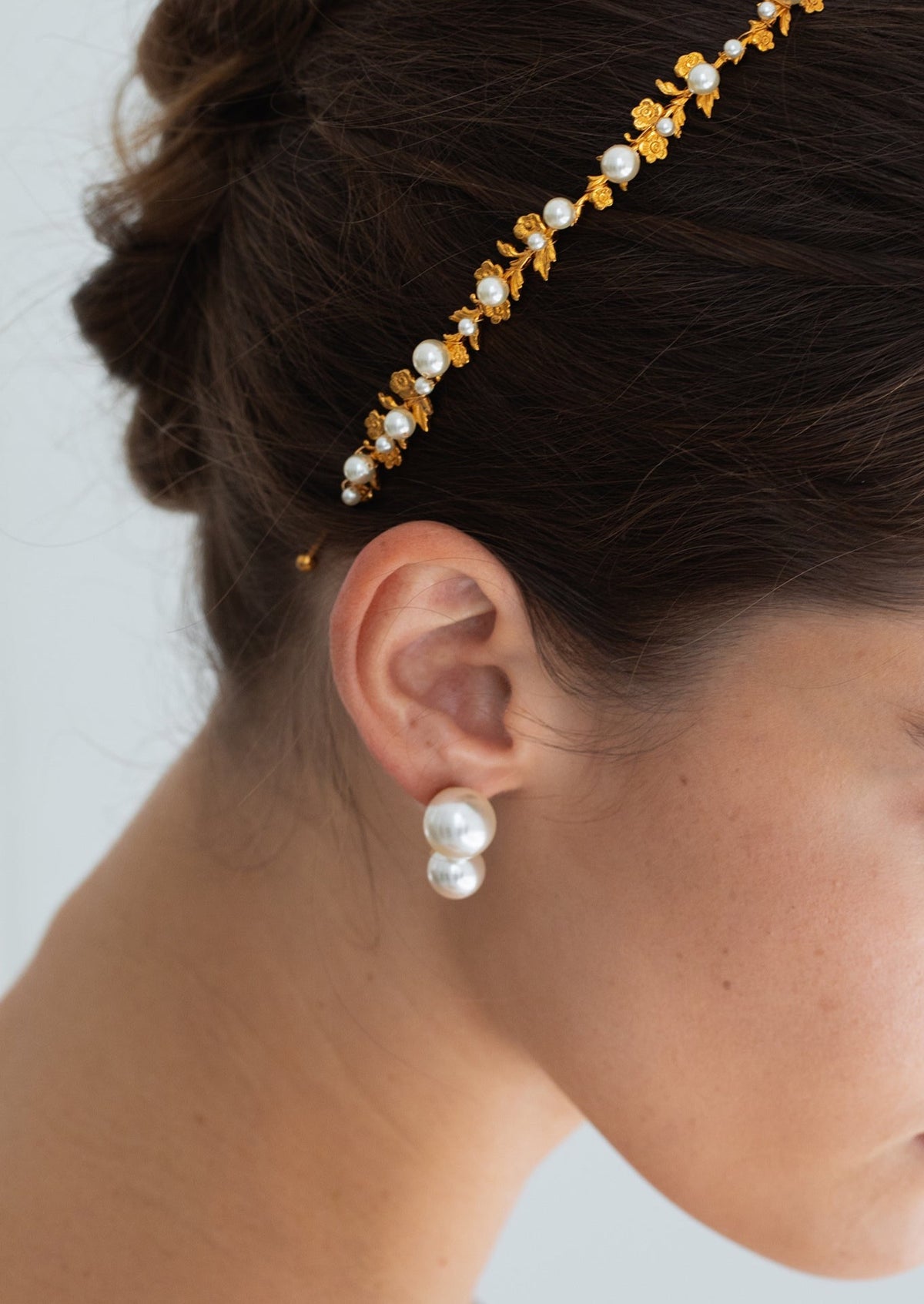 Close-up side view of Mae Headband in Gold Pearl showcasing 18K gold-plated flowers and pearl details on dark hair