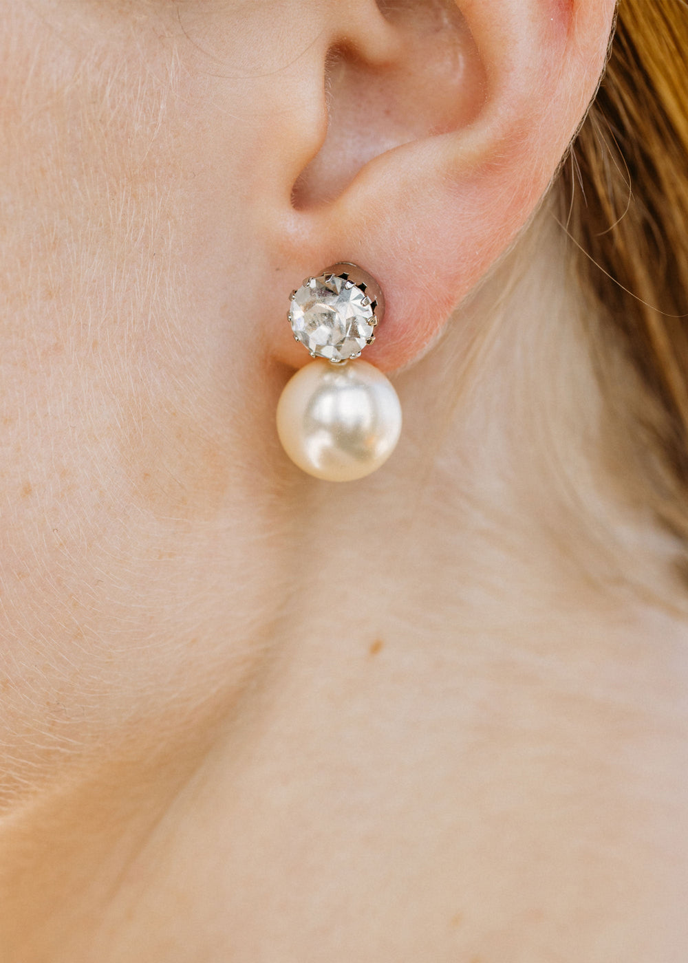 Close up of Ines earrings on ear showing faceted crystal stud with dangling pearl against skin background