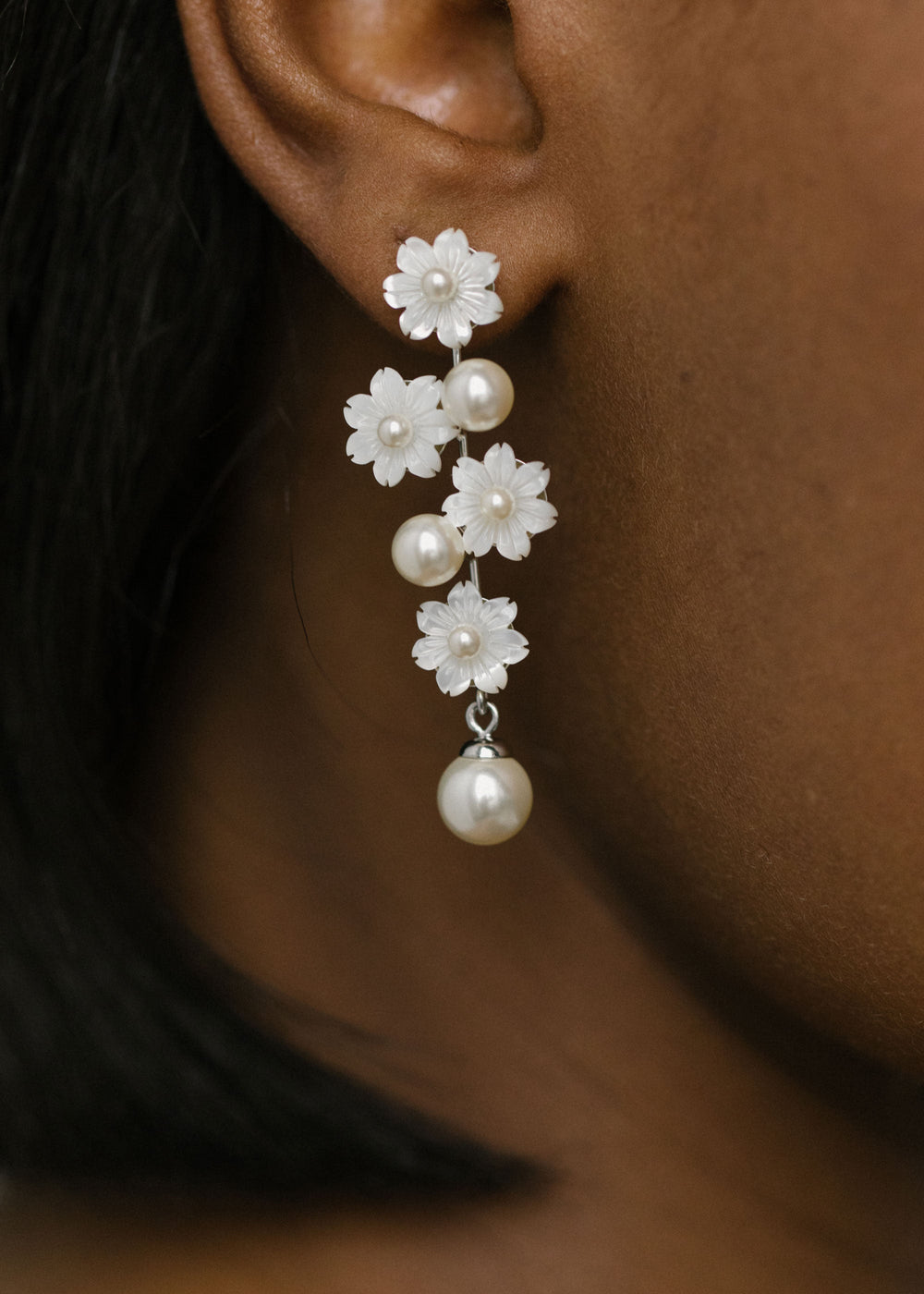 Close-up side view of Calissa earring showcasing hand-carved mother-of-pearl flowers and dangling pearls on a model’s ear