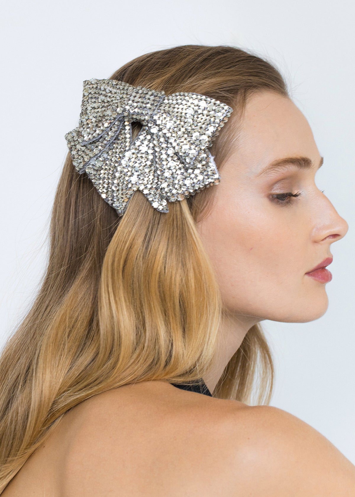 Close up side view of Belle Bow Barrette showcasing hand embroidered crystals worn in brown hair against a light background
