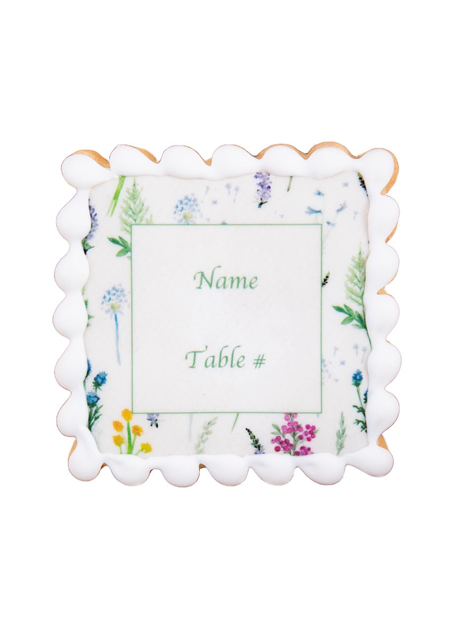 Front view of name-plate cookie with edible floral print, scalloped icing border, showing demo text Name and Table number