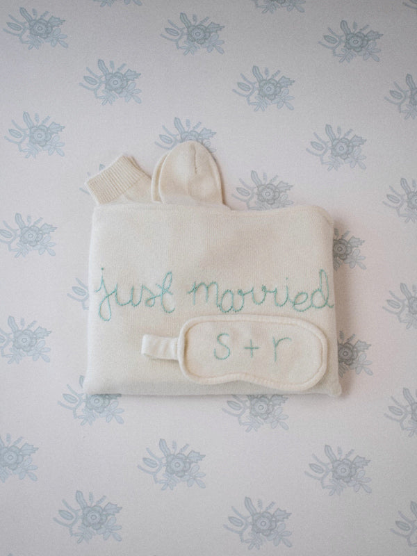 Flat lay of cream travel set with embroidered just married, monogrammed eye mask S plus R, and matching socks