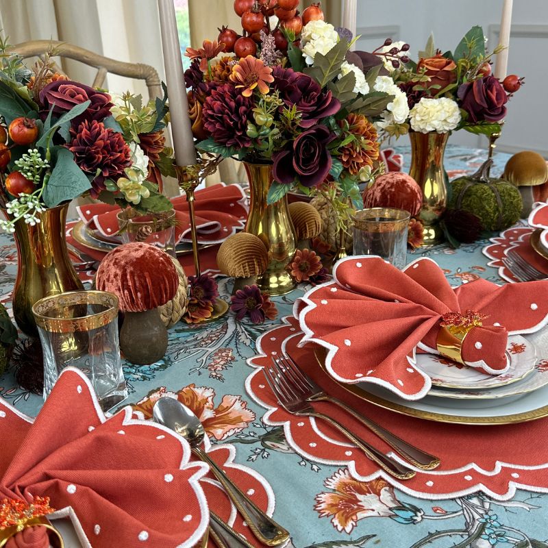 Teal blue tablecloth with gray and white branches, orange and wine flowers and green leaves, and orange placemats and matching napkins