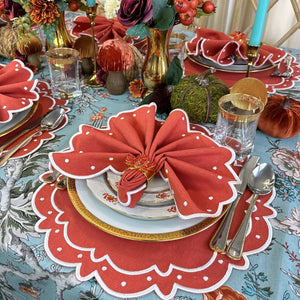 Teal blue tablecloth with gray and white branches, orange and wine flowers and green leaves, and orange placemats and matching napkins