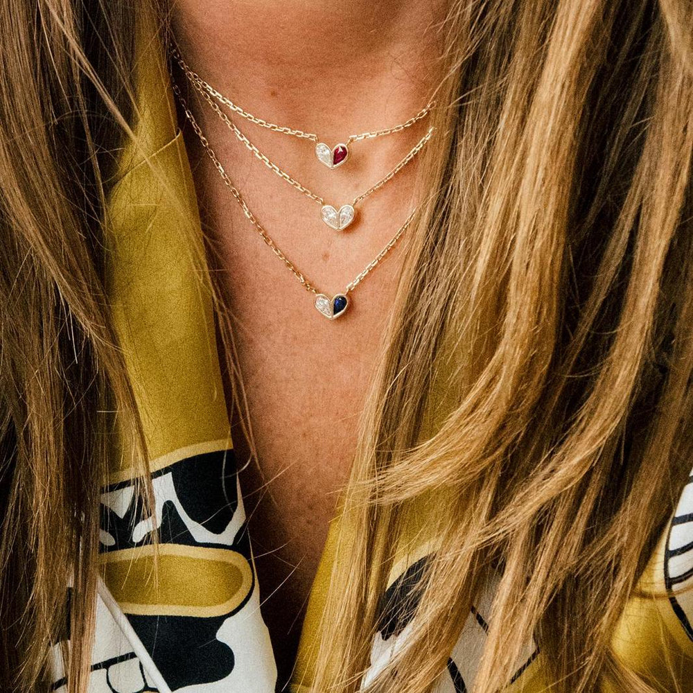 Close-up of Sweetheart Necklace in Diamond: layered gold chains with diamond heart pendants, red and blue accents on model